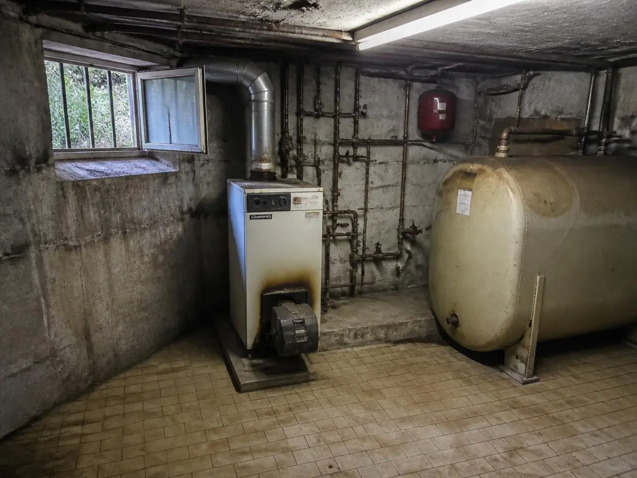 Chaufferie en sous-sol : vieille chaudière au fioul, traces de suie autour du brûleur, cuve et conduit de fumée.