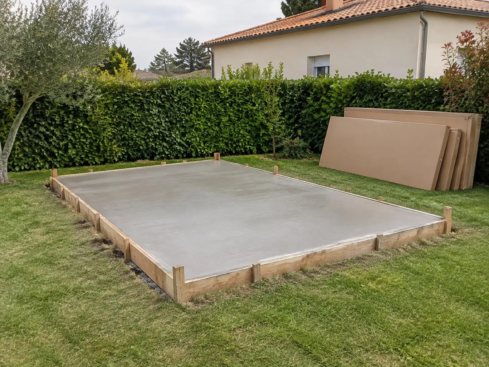 Dalle en béton fraîchement coulée, lisse et de niveau dans son coffrage en planches, sur la pelouse d’un jardin.
